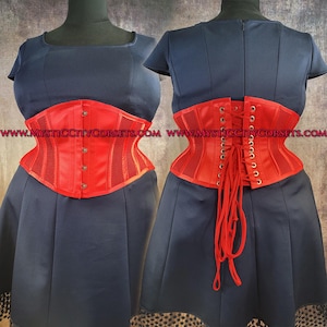 May include: A red corset with a mesh center panel and a satin finish, displayed on a mannequin. The corset has a button-up front and a lace-up back. The corset is worn over a navy blue dress.