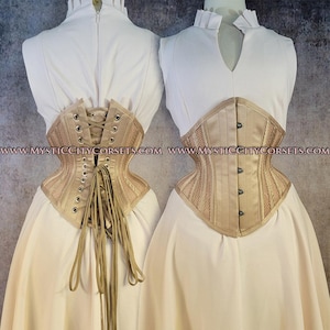 May include: Two beige corsets are displayed, showcasing their intricate design. The corsets feature a structured silhouette with boning, eyelets for lacing, and a satin-like finish. One corset is laced up, while the other is buttoned. The corsets are paired with white dresses.