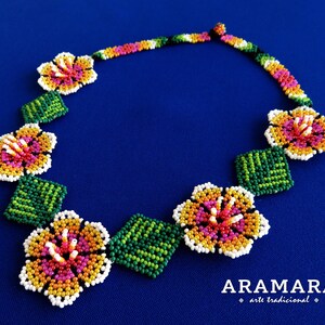 May include: A beaded necklace with a floral design. The necklace is made with white, yellow, orange, pink, and green beads. The necklace is on a blue background. The text "ARAMARA arte tradicional" is at the bottom of the image.