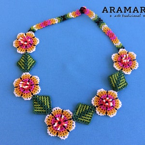 May include: A beaded necklace with a floral design. The necklace is made of small, colorful beads in shades of orange, yellow, pink, green, and white. The flowers are arranged in a symmetrical pattern, with leaves in between each flower.