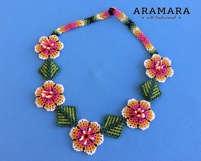 May include: A beaded necklace with a floral design. The necklace is made of small, colorful beads in shades of orange, yellow, pink, green, and white. The flowers are arranged in a symmetrical pattern, with leaves in between each flower.