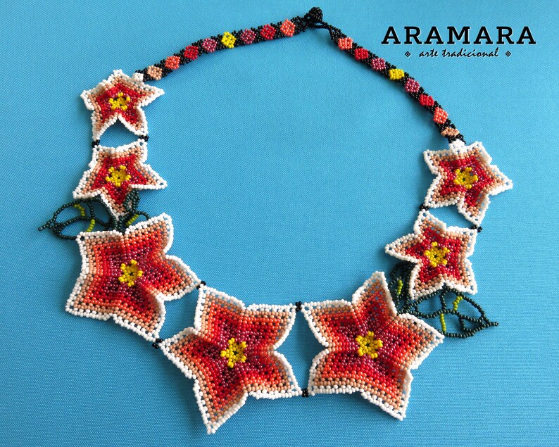 May include: A beaded necklace with a floral design. The necklace is made of white, red, orange, yellow, and green beads. The necklace is called "Aramara arte tradicional".
