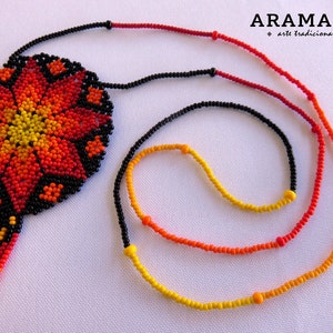 May include: A beaded necklace with a large, colorful flower pendant. The pendant is made of black, red, orange, and yellow beads. The necklace is made of black, red, orange, and yellow beads. The necklace is called "Aramara" and is described as "arte tradicional".