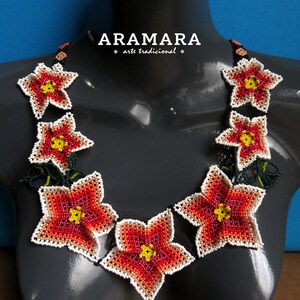 May include: A necklace made of red, white, and yellow beaded flowers. The necklace is on a gray mannequin and the text "ARAMARA arte tradicional" is above the necklace.