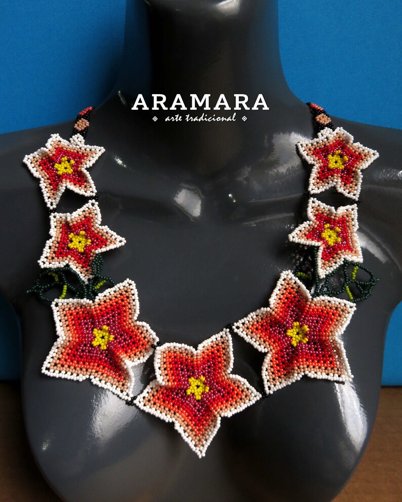 May include: A necklace made of red, white, and yellow beaded flowers. The necklace is on a gray mannequin and the text "ARAMARA arte tradicional" is above the necklace.