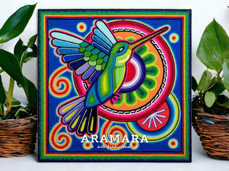 May include: A colourful, hand-painted artwork depicting a hummingbird in flight. The hummingbird is surrounded by concentric circles of vibrant colours, including red, orange, yellow, green, blue, and purple. The artwork is signed "ARAMARA arte tradicional" in the bottom centre.