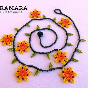 May include: A beaded necklace with a dark blue base and orange, yellow, and green flower accents. The necklace is made with small beads and features a repeating pattern of flowers and leaves. The necklace is called "Aramara arte tradicional".