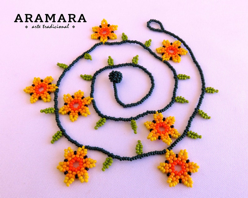 May include: A beaded necklace with a dark blue base and orange, yellow, and green flower accents. The necklace is made with small beads and features a repeating pattern of flowers and leaves. The necklace is called "Aramara arte tradicional".