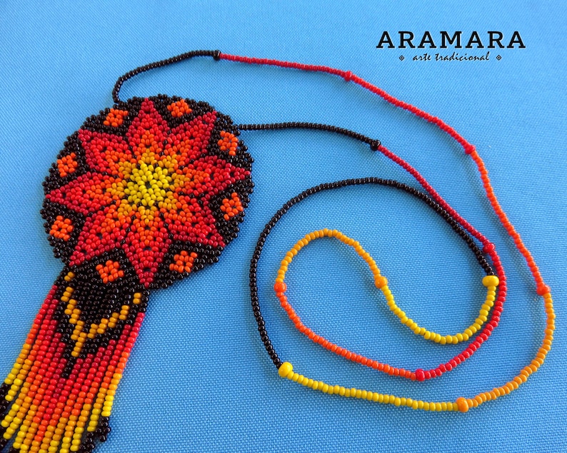 May include: A beaded necklace with a large, round pendant featuring a colorful geometric design in shades of red, orange, and yellow. The pendant is attached to a black beaded cord with a fringe of red, orange, and yellow beads.