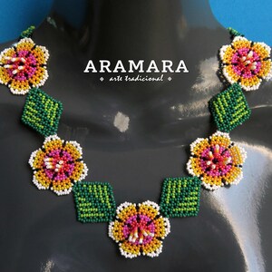 May include: A beaded necklace with a floral design. The necklace features white, yellow, pink, and green beads arranged in the shape of flowers and leaves. The necklace is on a gray mannequin.