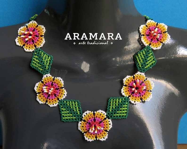 May include: A beaded necklace with a floral design. The necklace features white, yellow, pink, and green beads arranged in the shape of flowers and leaves. The necklace is on a gray mannequin.