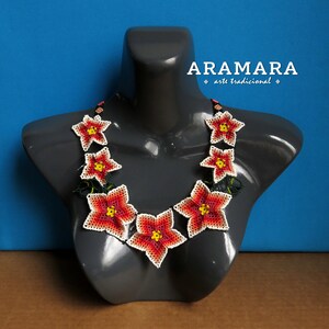 May include: A beaded necklace with red, yellow, and white flowers. The necklace is on a gray mannequin and the text "ARAMARA arte tradicional" is above the necklace.