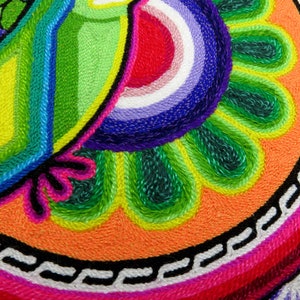 May include: A colourful circular tapestry with a green, blue and yellow design in the top left corner. The design is surrounded by a ring of green, orange and pink. The centre of the tapestry is a circle of pink with a white and black chain design.