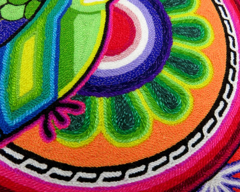 May include: A colourful circular tapestry with a green, blue and yellow design in the top left corner. The design is surrounded by a ring of green, orange and pink. The centre of the tapestry is a circle of pink with a white and black chain design.
