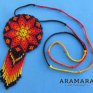 May include: A beaded necklace with a large, round pendant featuring a red, orange, and yellow flower design. The pendant is attached to a black beaded fringe. The necklace is made of black, red, orange, and yellow beads.