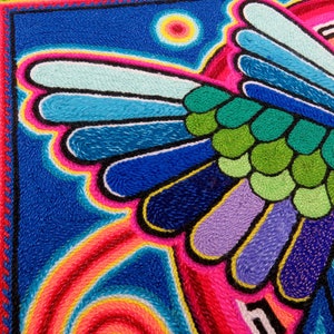 May include: A colourful embroidered artwork depicting a bird with vibrant blue, green, purple, and pink feathers. The background is a dark blue with a yellow sun.