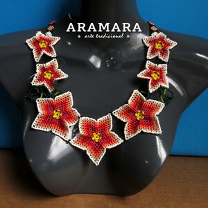 May include: A necklace made of red, white, and yellow beaded flowers. The necklace is on a gray mannequin and the background is blue. The text "ARAMARA arte tradicional" is on the necklace.