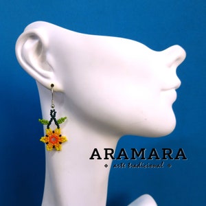 May include: A pair of beaded earrings with a yellow, orange, and red flower design. The earrings are hanging from a silver hook and have green leaves.