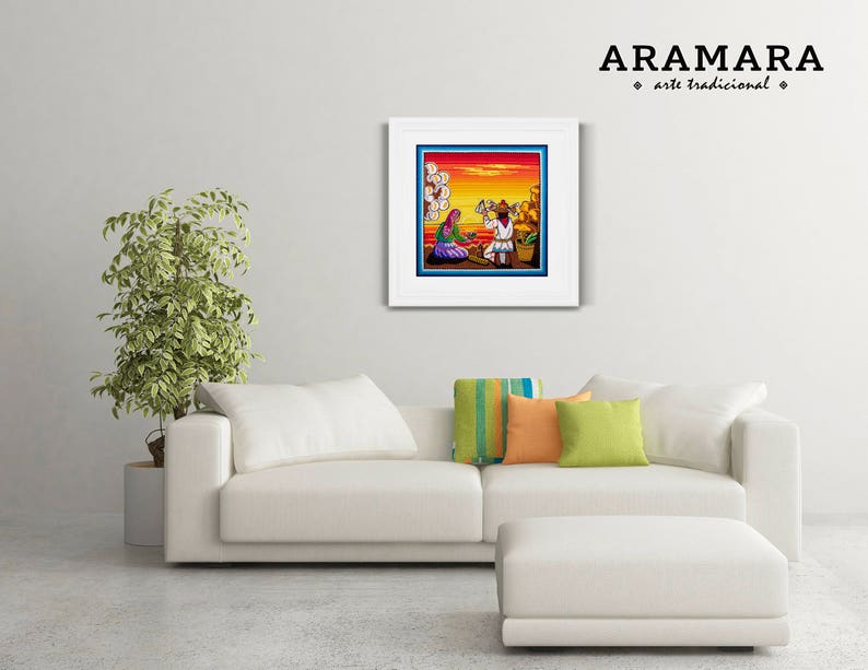 May include: A framed artwork depicting a colorful scene with two figures in traditional clothing. The artwork is titled "ARAMARA arte tradicional" and is displayed on a white wall above a white couch with pillows.