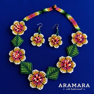 May include: A beaded necklace and earrings set featuring colorful flower designs. The necklace has five flowers with green leaves in between. The earrings are a matching pair of flowers. The set is made with small, colorful beads and has a white background.