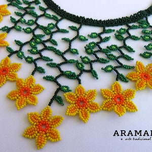 Op de afbeelding: Een kralenketting met een bloemmotief. De ketting heeft een donkergroene kralenbasis met groene kralenbladeren en geel-oranje kralenbloemen. De ketting is handgemaakt en heeft een delicate uitstraling.