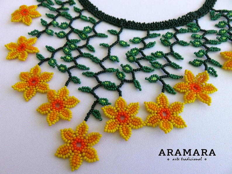 Op de afbeelding: Een kralenketting met een bloemmotief. De ketting heeft een donkergroene kralenbasis met groene kralenbladeren en geel-oranje kralenbloemen. De ketting is handgemaakt en heeft een delicate uitstraling.