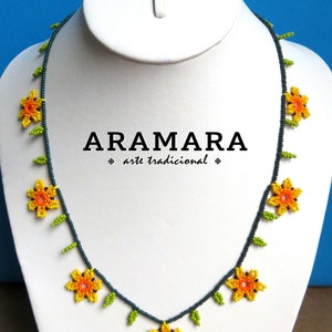 May include: A beaded necklace with a floral design. The necklace is made with dark blue beads and features yellow and orange flowers with green leaves. The necklace has the text "ARAMARA arte tradicional" on a white background.