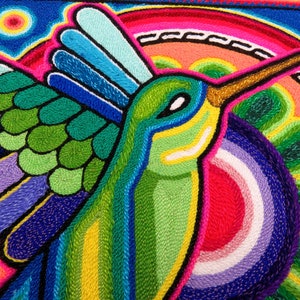 May include: A colourful embroidered hummingbird with green, blue, yellow and pink details. The hummingbird is flying with its wings spread out. The background is a vibrant blue with a pink and yellow sun.