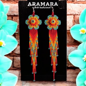 May include: A pair of long, beaded earrings with a flower design. The earrings are red, orange, yellow, and turquoise. The earrings are hanging from a black background.