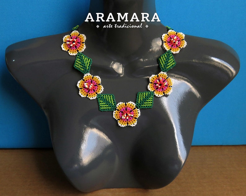 May include: A beaded necklace with a floral design. The necklace is made with white, pink, yellow, and green beads. The necklace is on a gray mannequin.