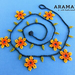 May include: A black beaded necklace with orange, yellow, and green flower accents. The necklace is made with small beads and has a delicate, feminine look. The necklace is labeled "ARAMARA * arte tradicional *"