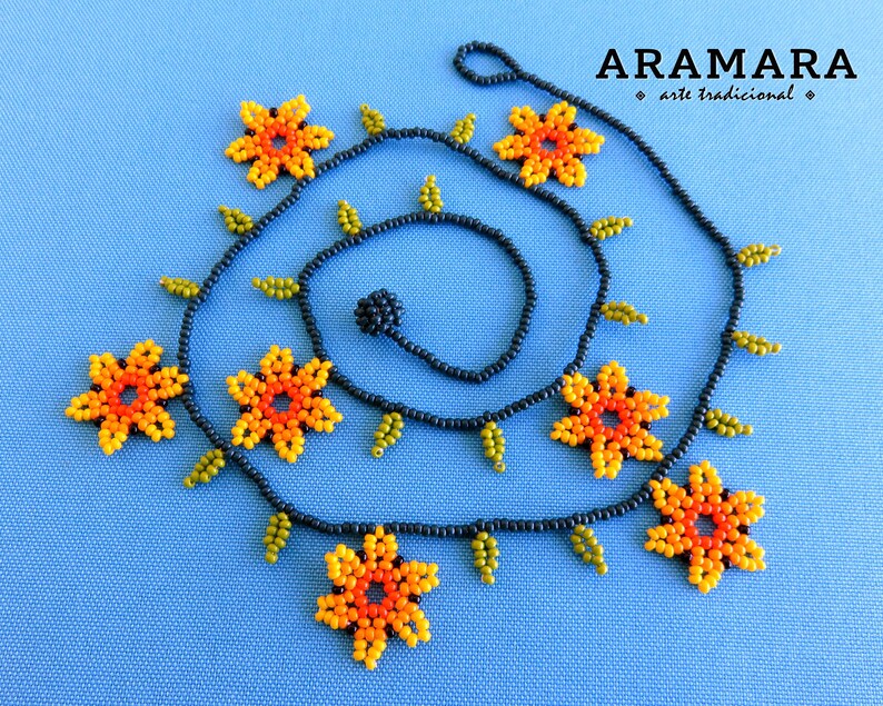 May include: A black beaded necklace with orange, yellow, and green flower accents. The necklace is made with small beads and has a delicate, feminine look. The necklace is labeled "ARAMARA * arte tradicional *"