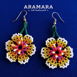 May include: A pair of beaded flower earrings with a green and silver hook. The flowers are made with white, yellow, orange, pink, and black beads.