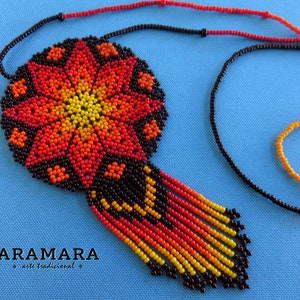 May include: A beaded necklace with a large, round pendant featuring a colorful flower design in shades of red, orange, and yellow. The pendant is surrounded by black beads and hangs from a black beaded chain.