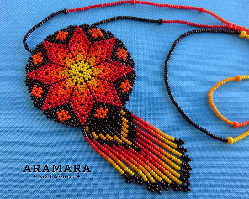 May include: A beaded necklace with a large, round pendant featuring a colorful flower design in shades of red, orange, and yellow. The pendant is surrounded by black beads and hangs from a black beaded chain.