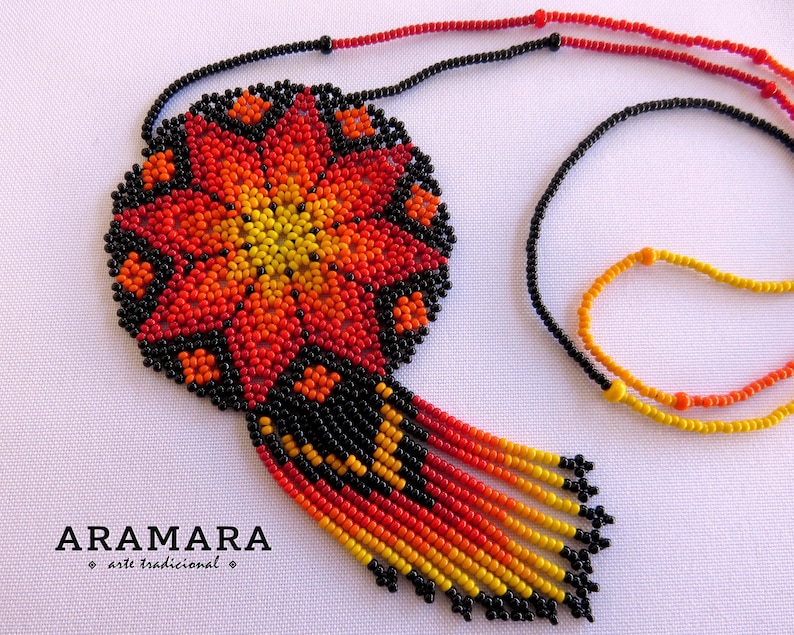 May include: A beaded necklace with a large, round pendant featuring a red, orange, and yellow flower design. The pendant is attached to a black beaded chain with a fringe of beads in the same colors.