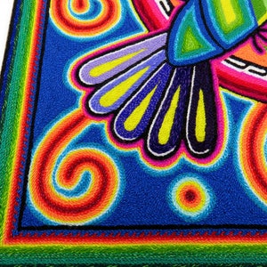 May include: A colourful embroidered artwork depicting a hummingbird with a blue body, green wings, and yellow accents. The background is a vibrant blue with swirling patterns in shades of red, orange, yellow, and white.