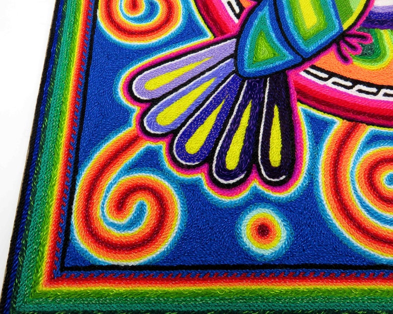 May include: A colourful embroidered artwork depicting a hummingbird with a blue body, green wings, and yellow accents. The background is a vibrant blue with swirling patterns in shades of red, orange, yellow, and white.