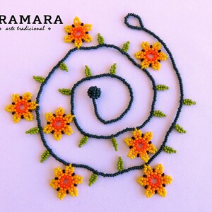 May include: A beaded necklace with a dark blue cord and yellow, orange, and green flower-shaped beads. The necklace is arranged in a spiral pattern.