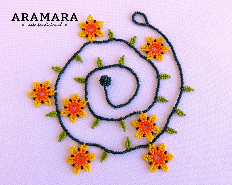 May include: A beaded necklace with a dark blue cord and yellow, orange, and green flower-shaped beads. The necklace is arranged in a spiral pattern.