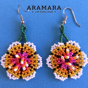 May include: A pair of beaded earrings with a flower design. The flowers are made of white, orange, yellow, pink, and black beads. The earrings are hanging from green beaded chains.
