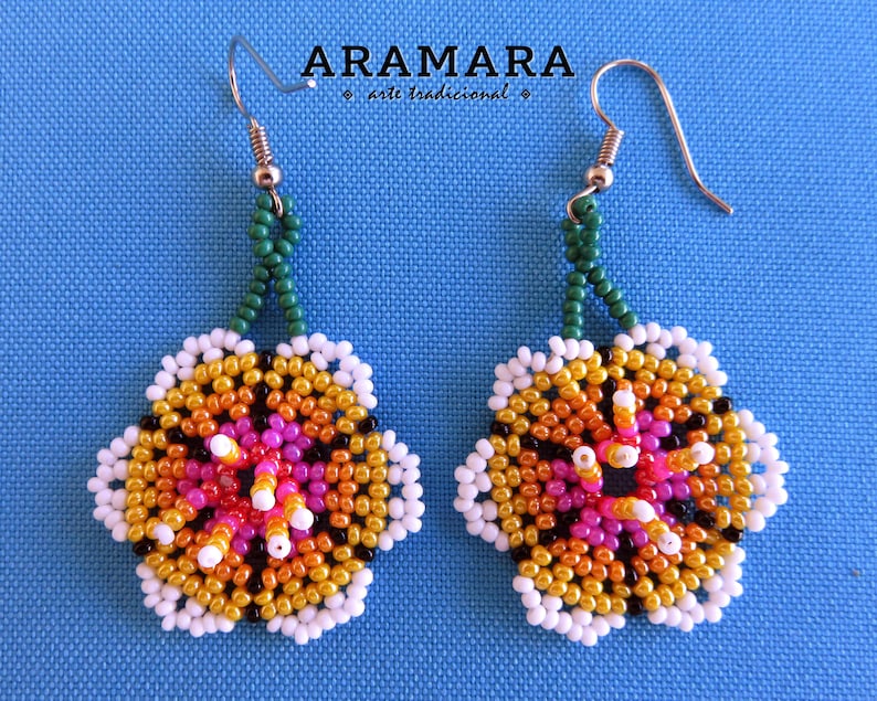 May include: A pair of beaded earrings with a flower design. The flowers are made of white, orange, yellow, pink, and black beads. The earrings are hanging from green beaded chains.