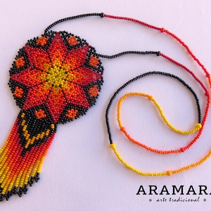 May include: A beaded necklace with a large, round pendant featuring a colorful flower design in shades of red, orange, and yellow. The pendant is attached to a black beaded chain.