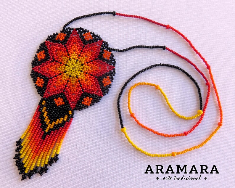 May include: A beaded necklace with a large, round pendant featuring a colorful flower design in shades of red, orange, and yellow. The pendant is attached to a black beaded chain.