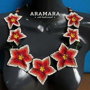 May include: A beaded necklace with a floral design. The necklace is made of small, colorful beads and features a series of red, orange, and white flowers. The flowers are arranged in a circular pattern around the neck. The necklace is on a gray mannequin.