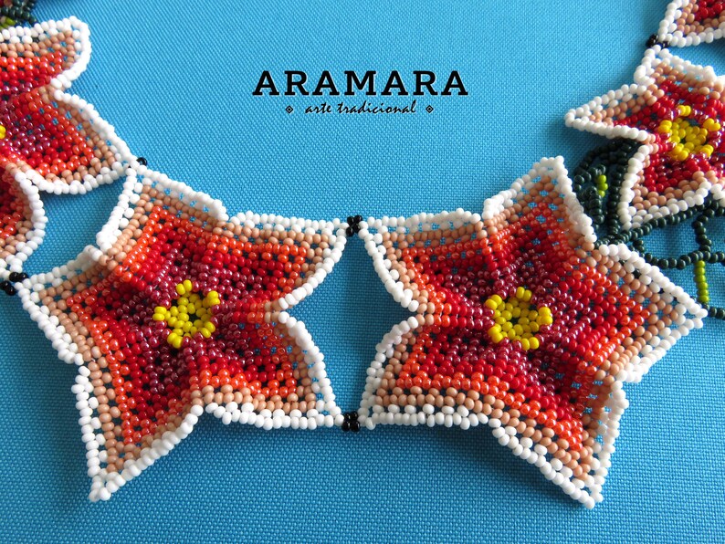 May include: A close-up of a beaded necklace with a star-shaped flower design. The necklace is made of red, orange, yellow, and white beads. The text "ARAMARA arte tradicional" is visible in the background.