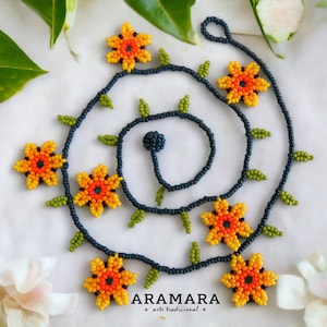 May include: A beaded necklace with a floral design. The necklace is made of dark blue beads and features orange, yellow, and green beads that form flowers. The necklace is on a white background.