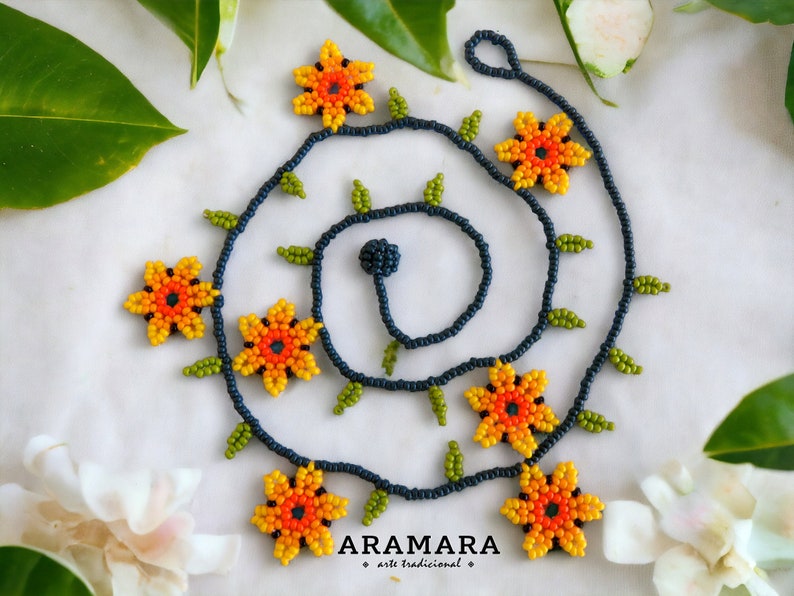 May include: A beaded necklace with a floral design. The necklace is made of dark blue beads and features orange, yellow, and green beads that form flowers. The necklace is on a white background.