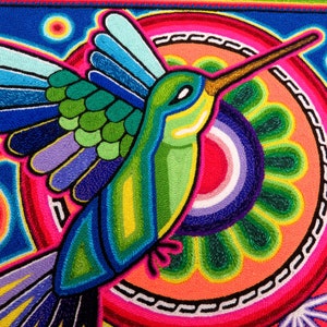 May include: A colourful embroidered artwork featuring a hummingbird with outstretched wings, flying over a circular design with concentric rings and a flower-like pattern.