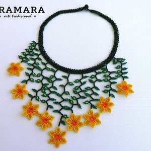 Op de afbeelding: Handgemaakte kralenketting met een zwarte kraag en een bloemmotief. De ketting heeft groene kralenranken en gele bloemen. De merknaam "ARAMARA" is linksboven zichtbaar. Een uniek sieraad.
